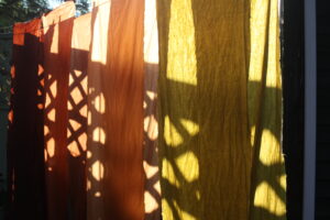 Yellow, orange, and red fabric glistens in the sun. Shadows from the fence make a pattern of diagonal lines.